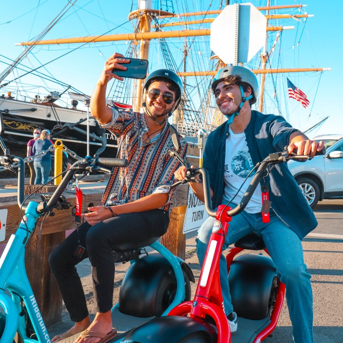 Two People Posing on Scooters in Front of Ship